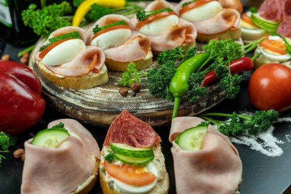 Delicious open-faced sandwiches with ham, eggs, and veggies on a wooden platter.