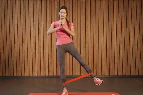 A woman performs leg exercises with a resistance band at a gym, promoting fitness and healthy living.